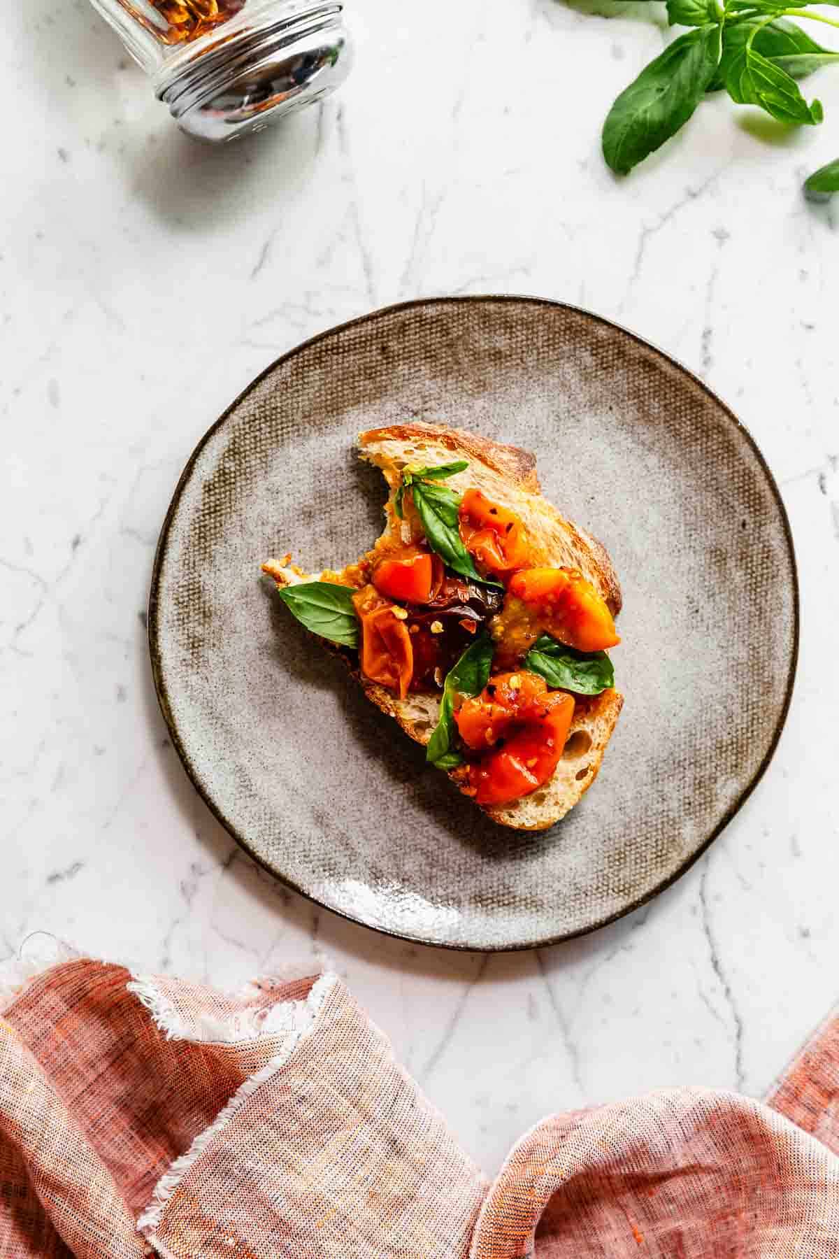 Air fryer cherry tomatoes and fresh basil on a plated bruschetta.