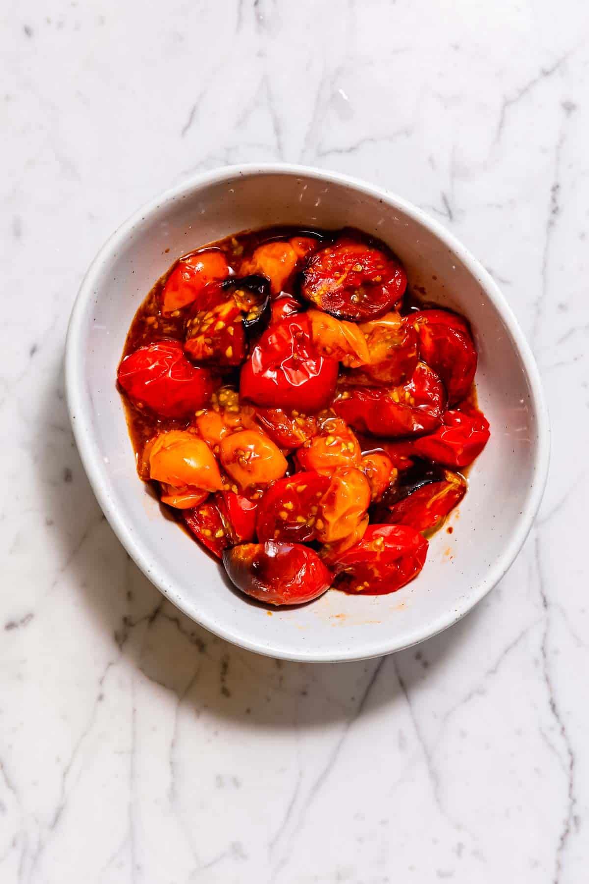 Cherry tomatoes roasted in an air fryer gathered in a white bowl on a marble counter.