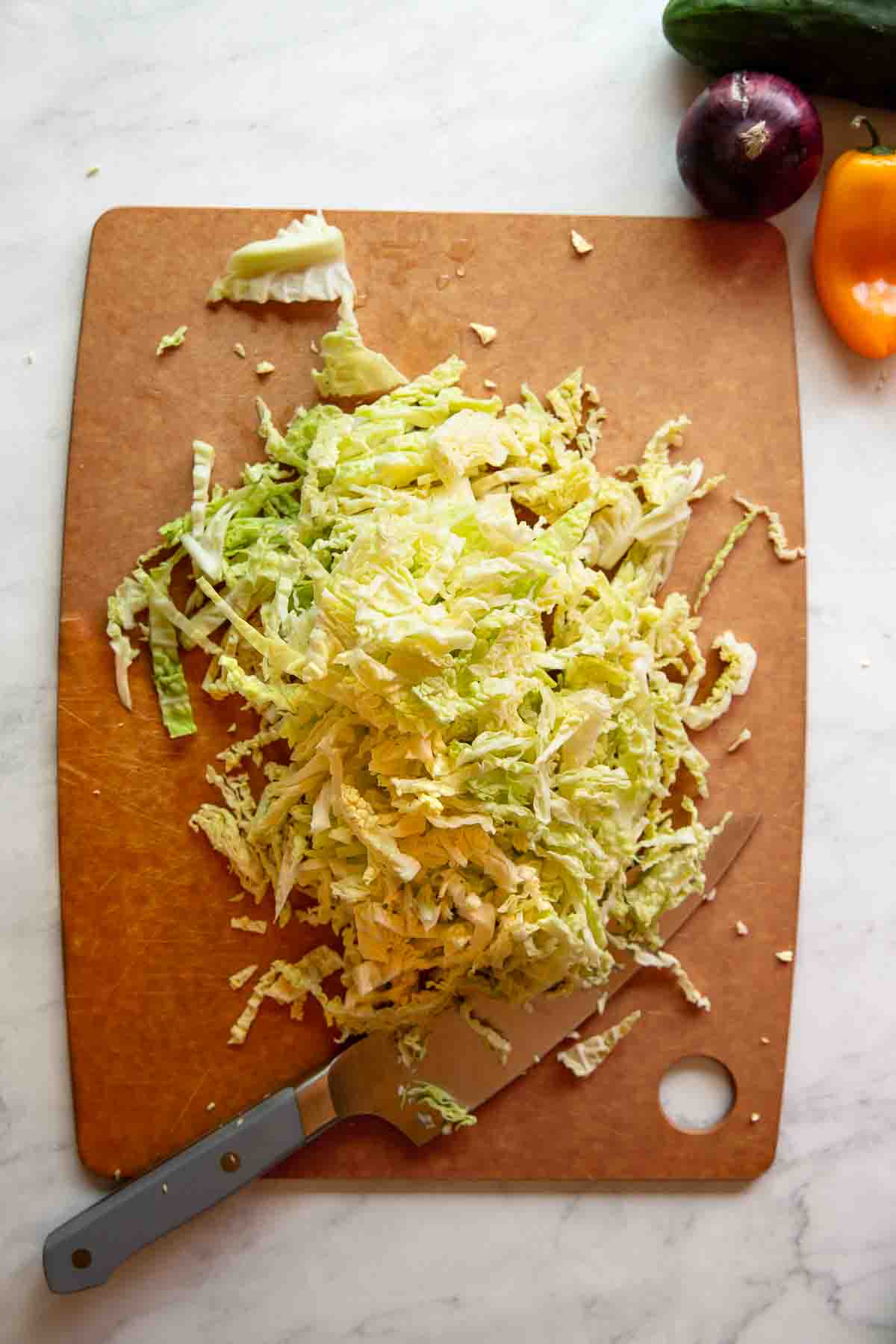 Sliced cabbage on a cutting board with a chef's knife and peppers surrounding it.