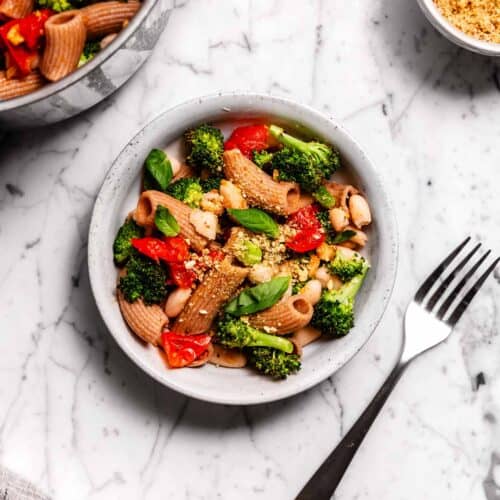 An overhead view of a bowl of broccoli and tomato pasta with beans.