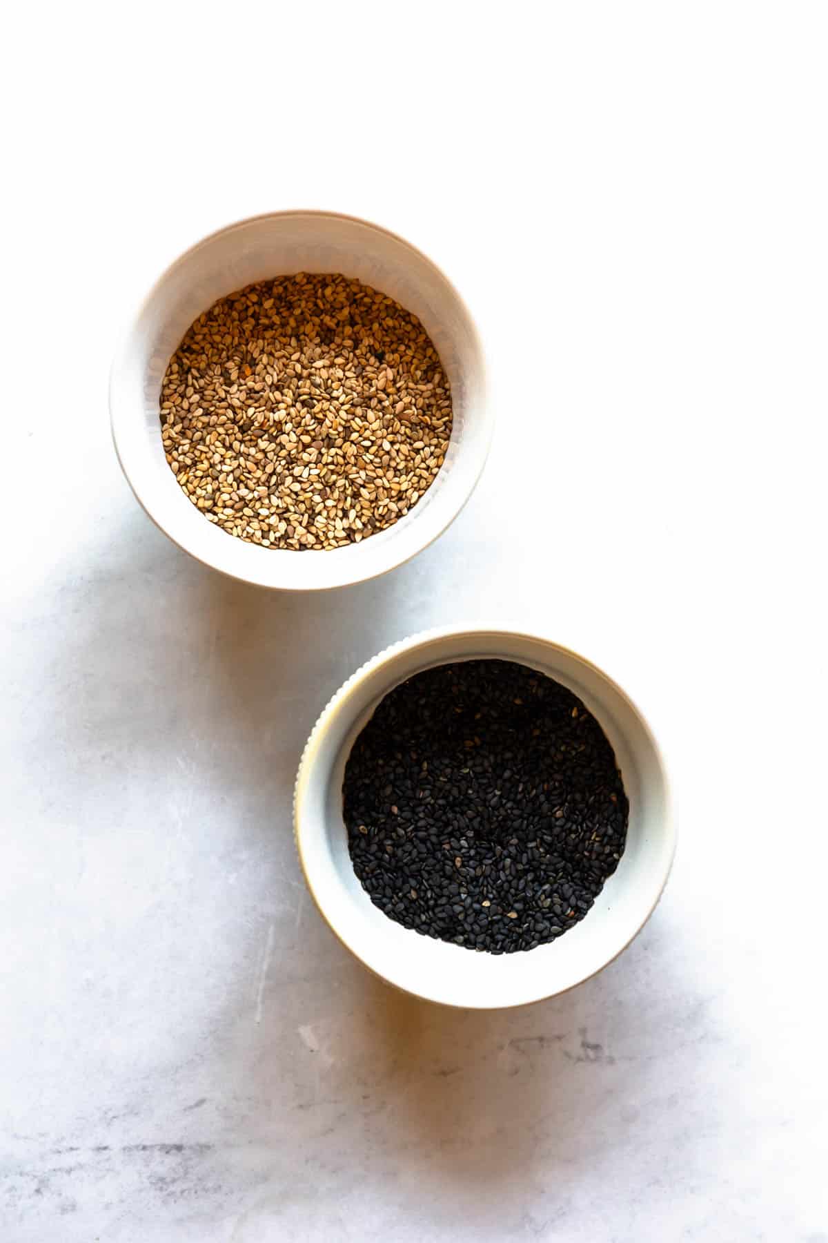 Two small bowls of sesame seeds, one with black seeds and one with white.
