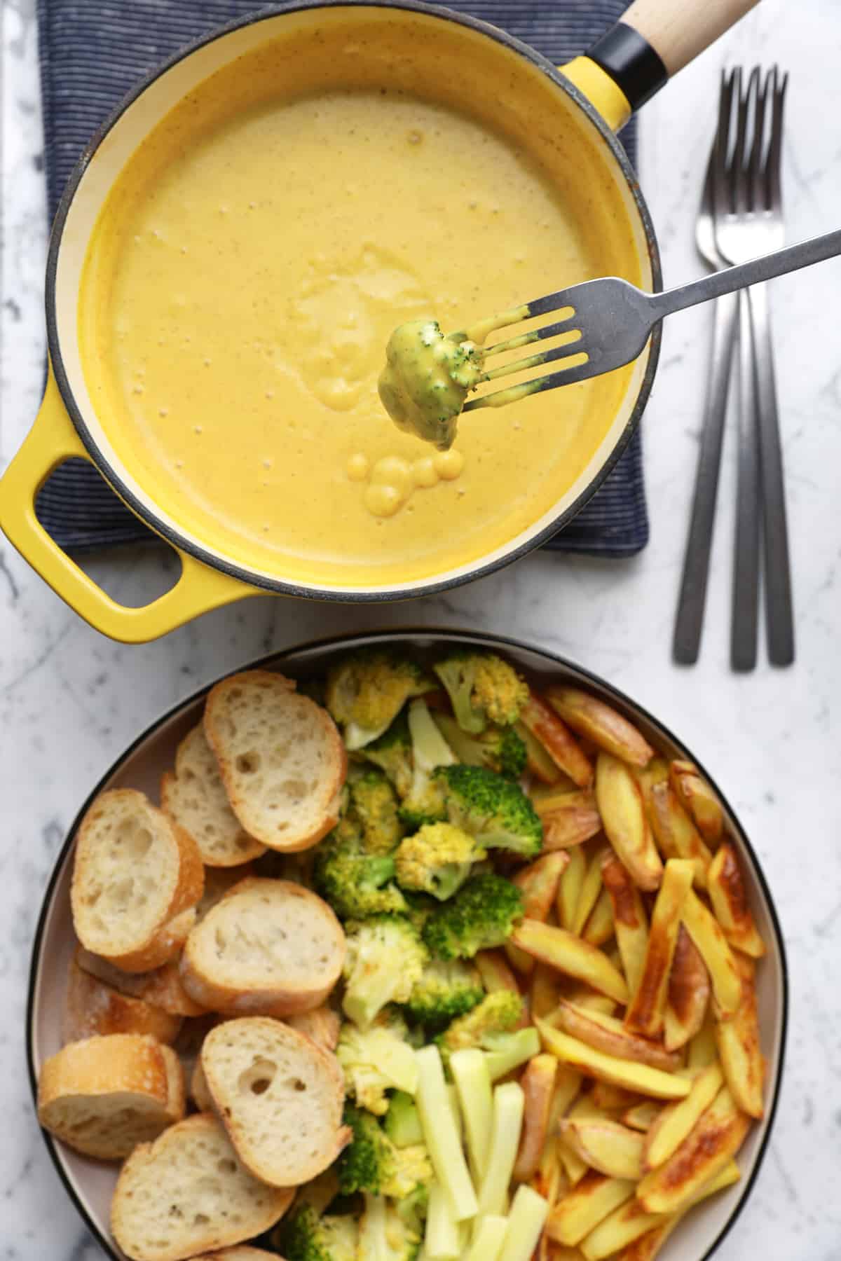 Roasted broccoli dipped into vegan fondue with a fork.