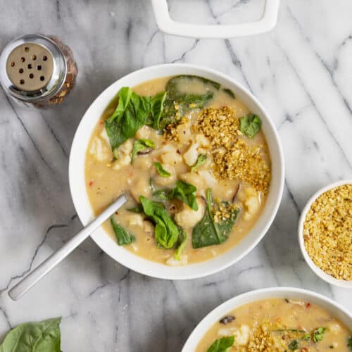 Two bowls of creamy gnocchi soup filled with cauliflower, beans, spinach, basil.