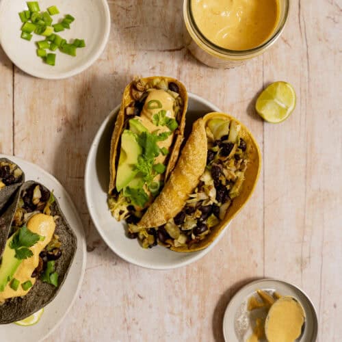 Black bean mushroom tacos with yellow corn tortillas on a light wood background.