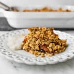 A plate of breakfast apple crisp sitting in front of a 9x13 that just came out of the oven.